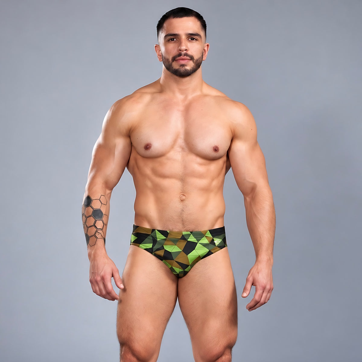 Modelo con traje de baño Brief Prisma de Equal Swimwear, estampado geométrico verde lima, oliva y negro, vista frontal.