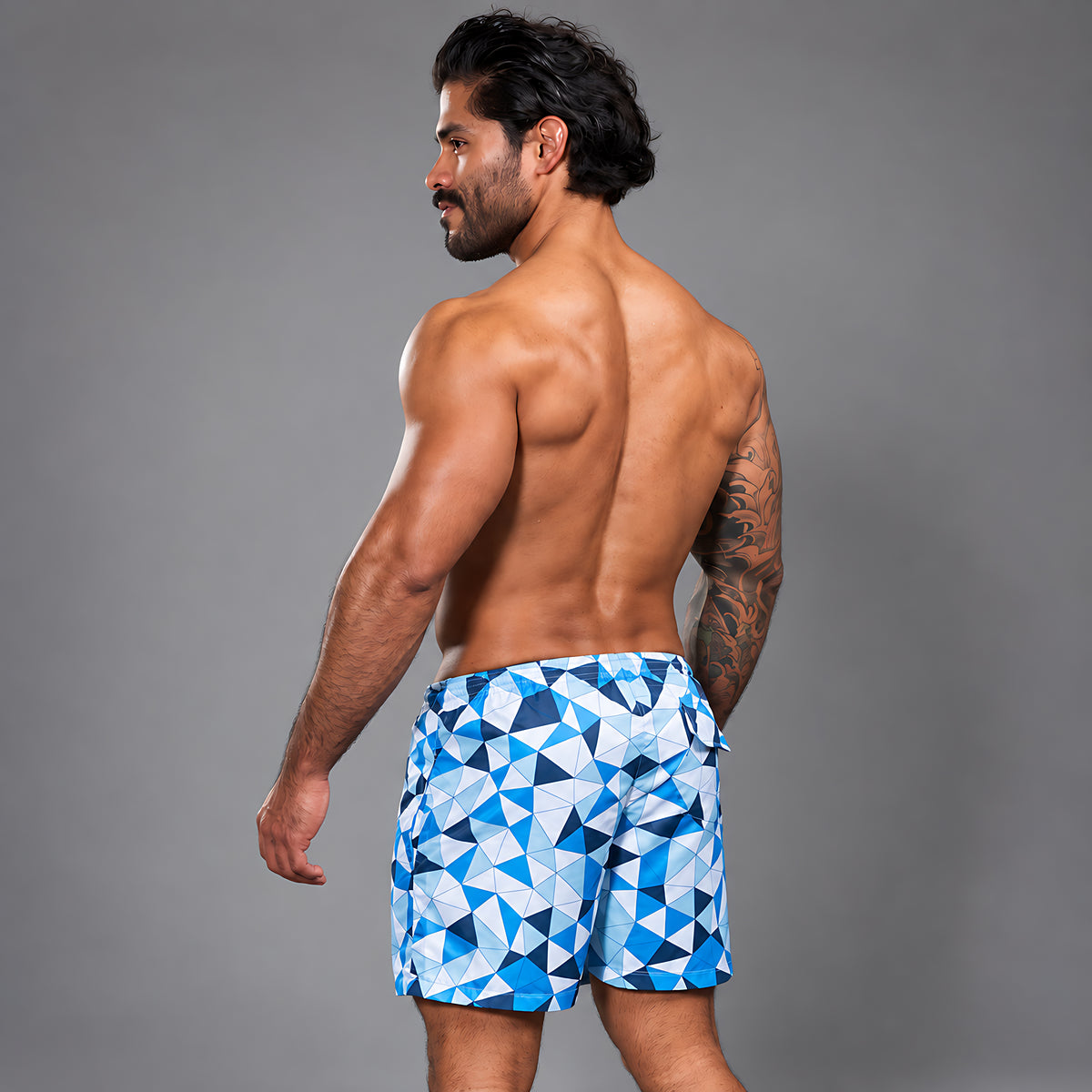 Modelo con Short Prisma Azul de Equal Swimwear, estampado de triángulos azules, celestes y blancos, vista trasera.