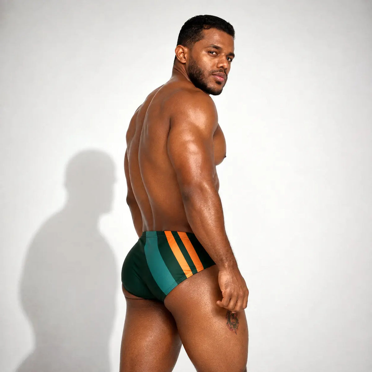 Brief de baño deportivo para hombre verde con franjas naranjas, vista posterior de tres cuartos – Brief Sport de EQUAL Swimwear