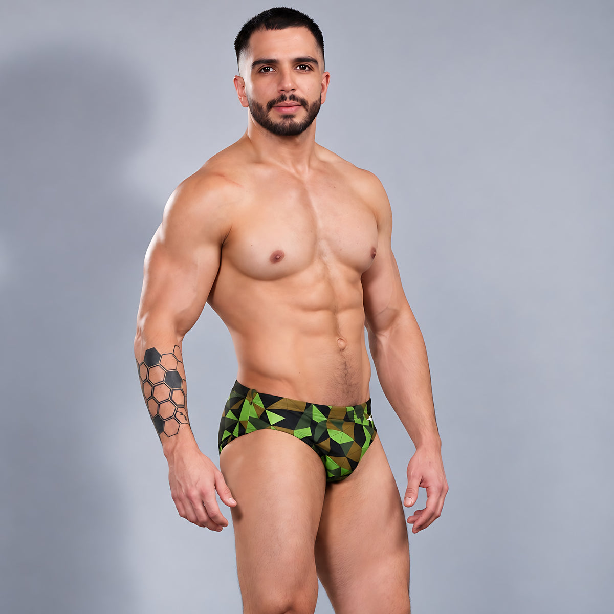 Modelo con traje de baño Brief Prisma de Equal Swimwear, estampado geométrico verde lima, oliva y negro, vista de tres cuartos.