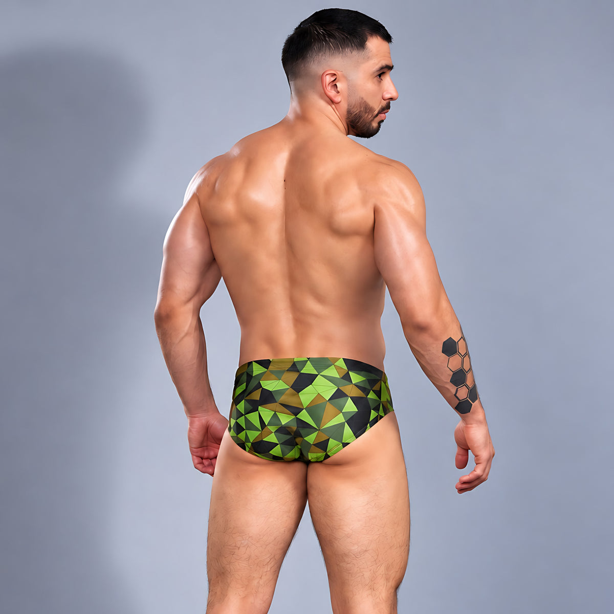 Modelo con traje de baño Brief Prisma de Equal Swimwear, estampado geométrico verde lima, oliva y negro, vista trasera.