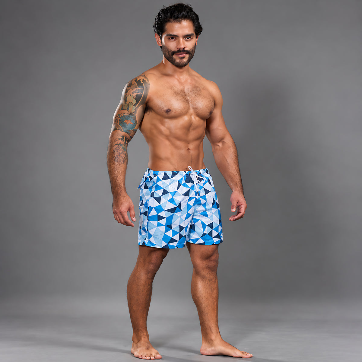 Modelo con Short Prisma Azul de Equal Swimwear, estampado de triángulos azules, celestes y blancos y cordón blanco, vista frontal.